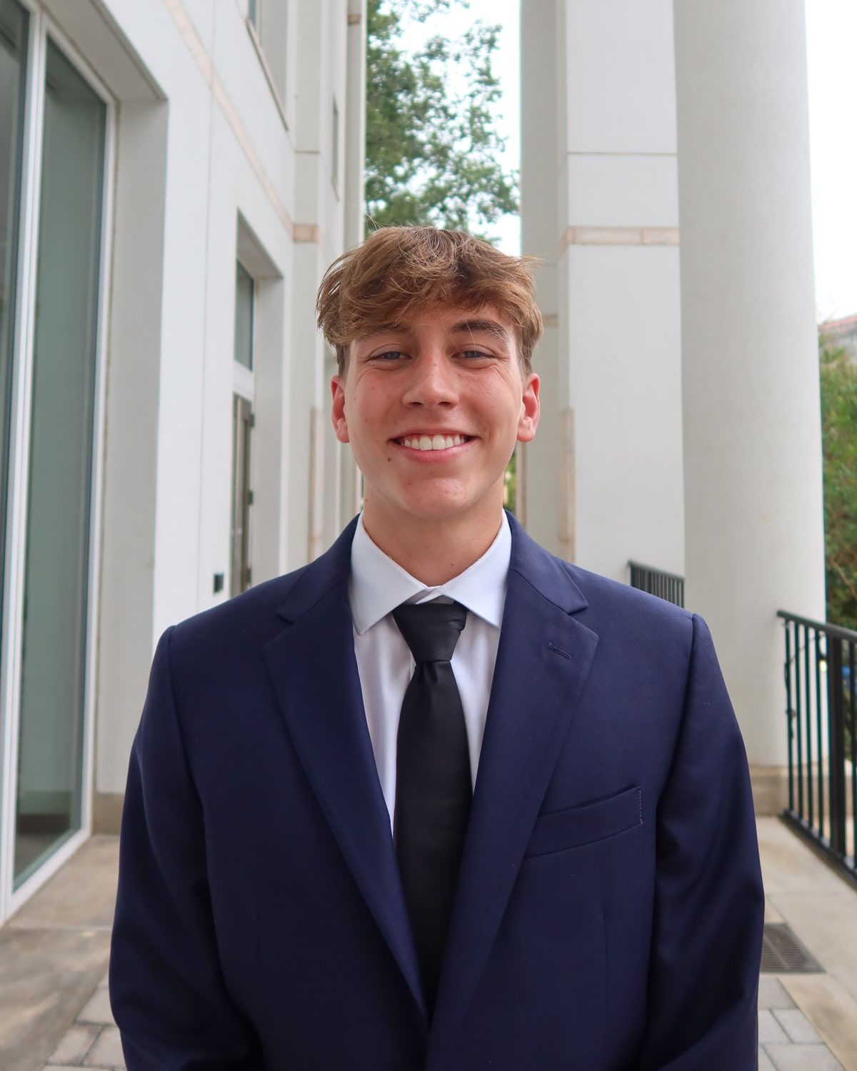 Connor May, in a navy suit, standing outside a pale stone building.