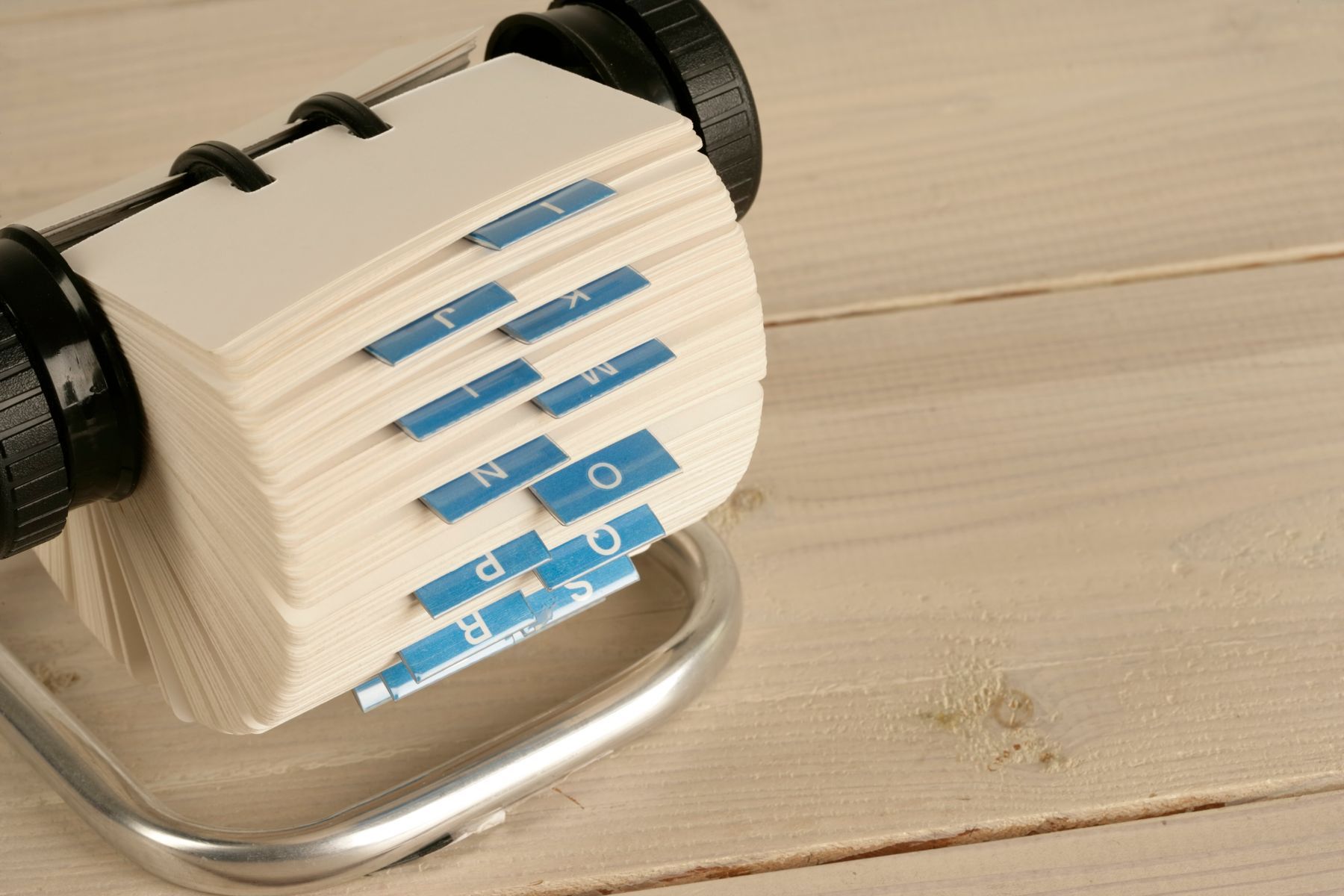 A rotary card file thick with cards, blue alphabet tabs sticking out of the stack, on pale wooden boards.