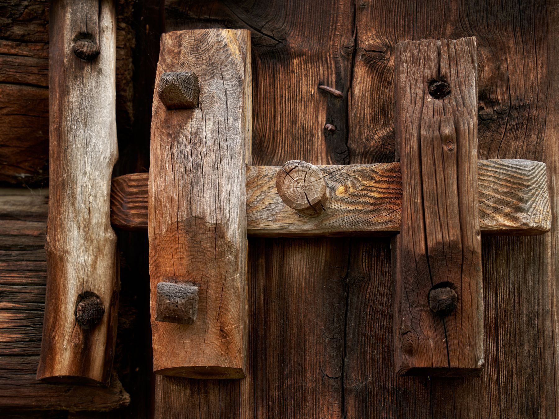 A heavy wooden bar latch across the planks of an old barn door, held shut by a single round peg, the timber weathered grey and brown.